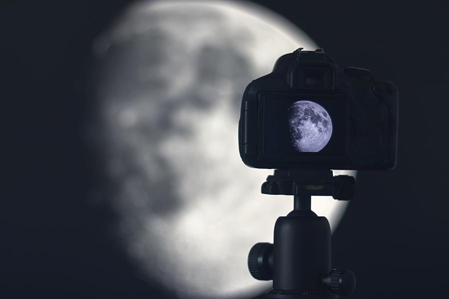 Moon photography. Camera with tripod capturing moon.